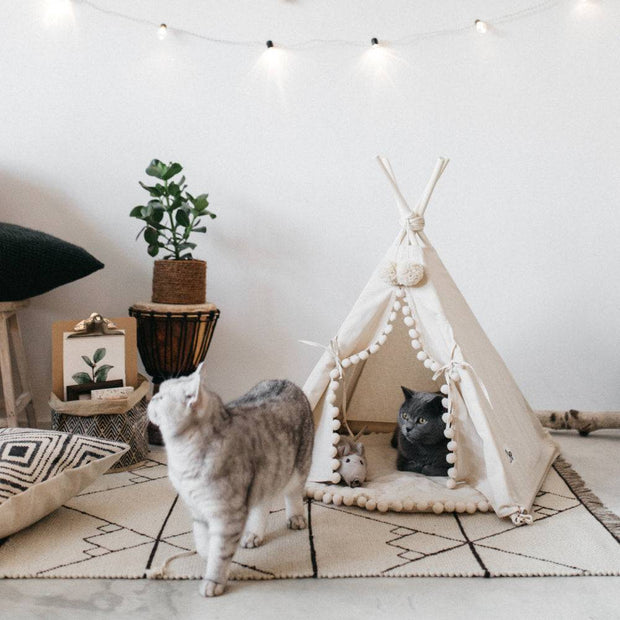 White pet teepee with wooden poles, a cozy spot for dogs and cats.
